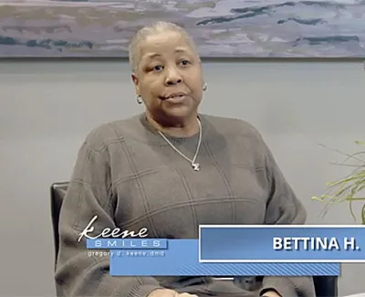 Woman named Bettina H. seated indoors with a plant and artwork in the background during an interview