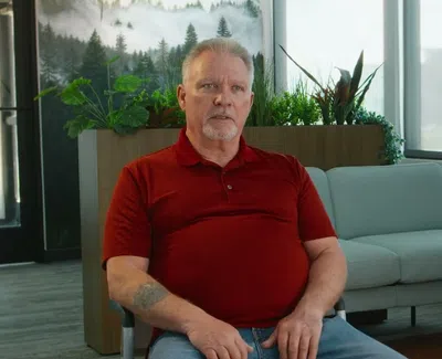 Man in red polo shirt sitting in modern living room with plants and window light during daytime