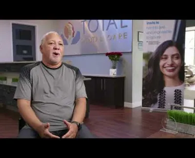 Middle-aged man speaking in a modern dental office with Total Foot Care sign and smiling woman banner.
