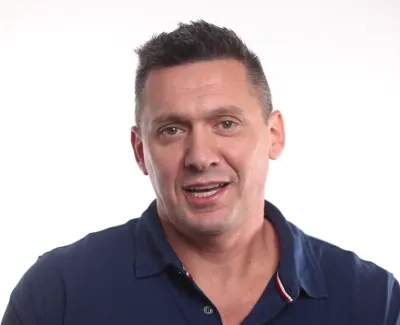 Smiling man with short dark hair wearing a navy blue polo shirt against a plain white background.