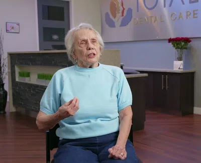 Elderly woman speaking in Total Dental Care office with dental signage and promotional banner in background
