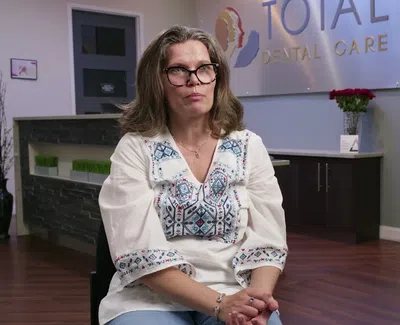 Middle-aged woman with glasses sitting in dental clinic Total Dental Care with promotional banner for Invisalign.