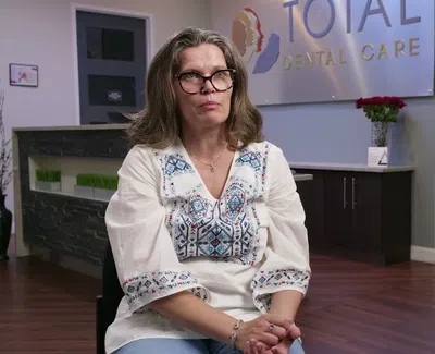 Middle-aged woman with glasses sitting in dental clinic Total Dental Care with promotional banner for Invisalign.