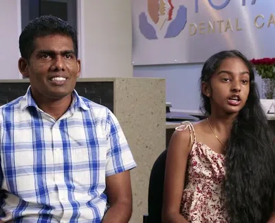 Man and girl sitting in a dental clinic reception area with a dental care sign in the background