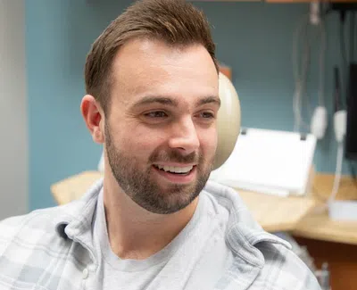 Smiling man sitting in a dental chair in a bright dental office with equipment in the background