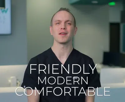 Male dental professional in black scrubs at modern clinic with words friendly, modern, comfortable overlayed.