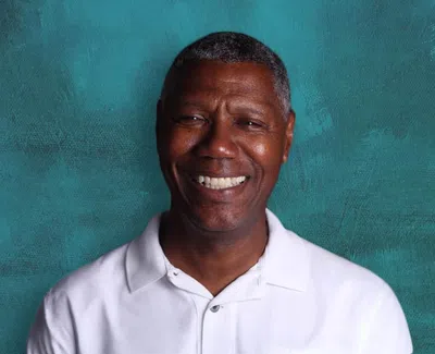 Smiling middle-aged man wearing a white polo shirt against a textured teal background