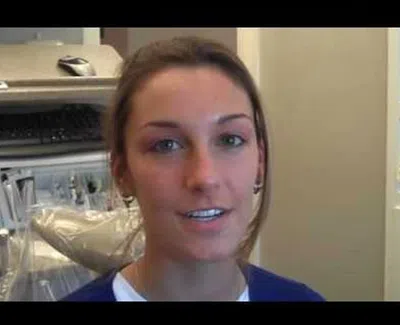 Young woman smiling in a dental office with dental chair and equipment in background.
