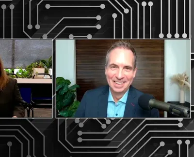 Two men in video call with black circuit board pattern background, one with long hair and another in blue suit.