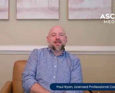 Licensed counselor Paul Ryan sitting on a brown leather chair in a room with light wall art and Ascend Medical logo.