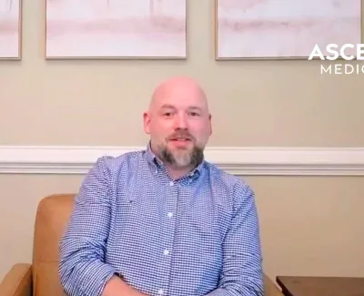 Man in blue checkered shirt sitting in a chair with Ascend Medical logo in background