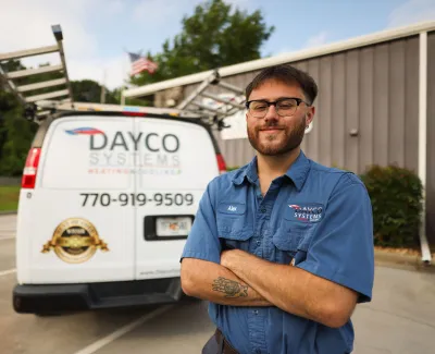 Dayco Systems technician with folded arms stands in front of a branded service van with ladders and phone number.