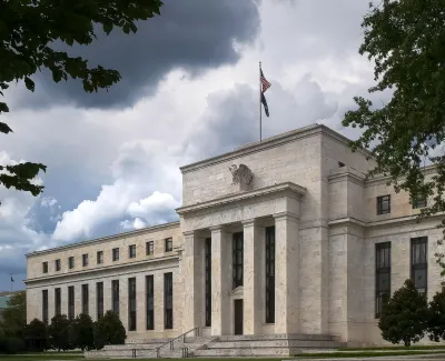 Historic Federal Reserve building with tall columns and an American flag under dramatic cloudy sky.
