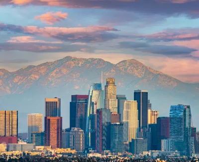 Los Angeles city skyline with tall skyscrapers and mountains under a colorful sunset sky.