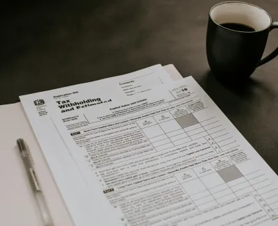 Tax forms and documents next to a pen and black coffee cup on a dark surface.