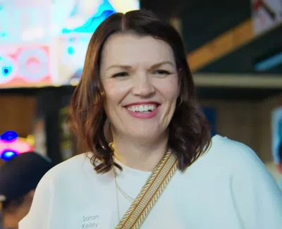 Smiling woman with brown hair and white top enjoys social setting in vibrant indoor environment.