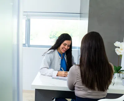 Female doctor in white coat smiles while discussing with patient in a bright medical office