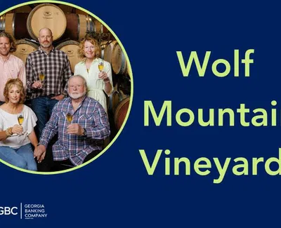 Five people holding wine glasses posing in front of wine barrels at Wolf Mountain Vineyards