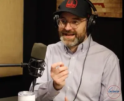 Man wearing headphones and cap speaking into a microphone in a podcast studio with soundproof panels.