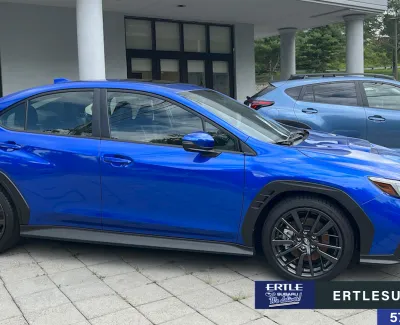 Side view of a vibrant blue Subaru compact car parked on a paved area outside a dealership building.