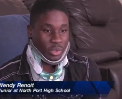 Young man wearing a neck brace being interviewed on a brown leather couch with blue caption overlay