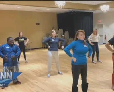 Group of diverse adults and teens standing with hands on hips in a spacious room during exercise or dance class.