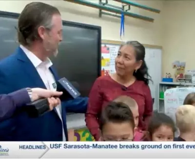 News reporter interviews woman in classroom full of young students with educational materials in background