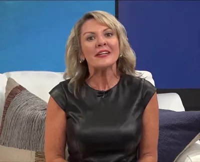 Blonde woman in black top sitting on a white couch with colorful pillows and a blue wall background