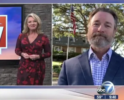 Television hosts presenting the Suncoast View show with logo on screen and outdoor interview with man in suit.