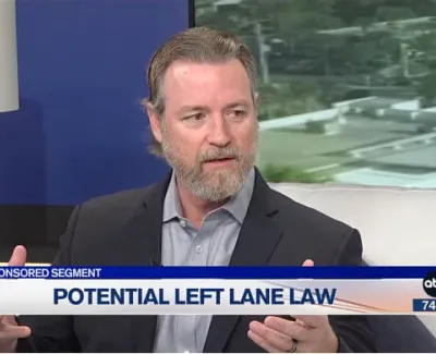 Man with beard discussing potential left lane law on a news segment with a blue background and lamp
