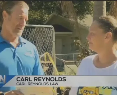 Carl Reynolds from Carl Reynolds Law talks to a woman outdoors near a fenced yard during a sunny day.