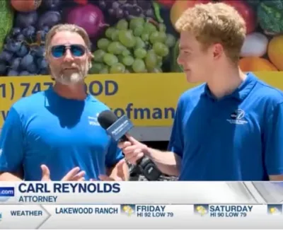 Attorney Carl Reynolds interviewed outdoors next to colorful fruit and vegetable truck background in blue shirts.