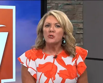 Female news anchor with blonde hair wearing white and orange floral dress presenting on ABC 7 news at 9:14 with temperature 82 degrees.