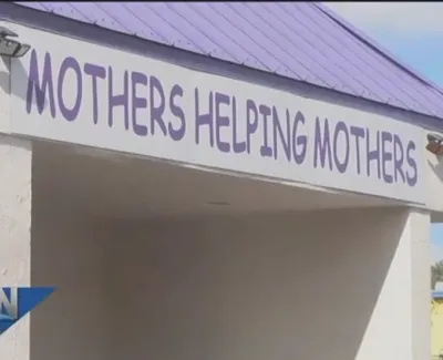 Building entrance with a sign that reads Mothers Helping Mothers under a purple roof and sunny sky.