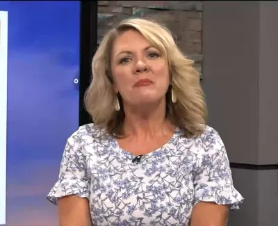Female news anchor in floral blouse presenting on a local TV station with temperature and time displayed
