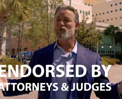 Man in suit speaking outdoors with text endorsed by attorneys and judges overlaid in front of building.