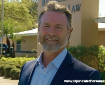 Smiling man in suit standing outside the law office of Campi Reynolds during a sunny day