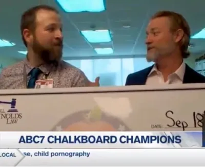 Two men holding a large check celebrating ABC7 Chalkboard Champions in an indoor office setting.