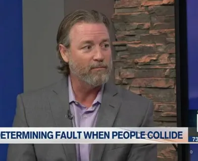 Man in gray suit and lavender shirt discusses determining fault in collisions on a news segment set.