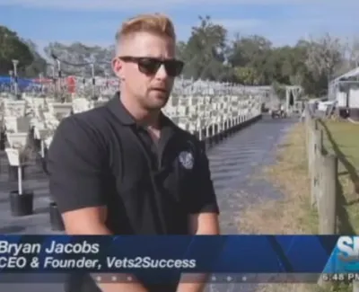 Man with sunglasses in black shirt stands near rows of potted plants outdoors under clear sky.