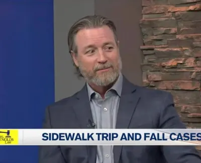 Man in gray suit discussing sidewalk trip and fall cases on local news station set.