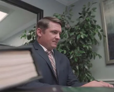Man in suit working at desk with large book in foreground and plant in office background