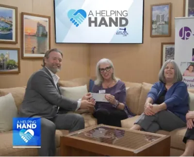Four people sitting in a living room setting exchanging a check for a charity named A Helping Hand supporting JoshProvides.org.