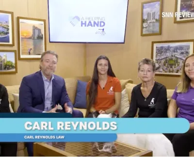 Five people seated in a studio setting with A Helping Hand logo and Carl Reynolds Law name displayed on screen.