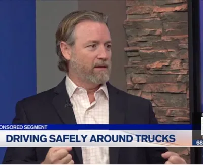 Man in blazer speaking during a sponsored TV segment about driving safely around trucks.