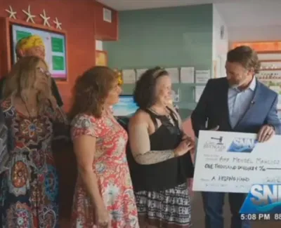 Group of women receiving a large donation check from a man in a suit inside a bright office space