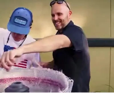 Two men smiling and making cotton candy together with a large cotton candy machine outdoors.