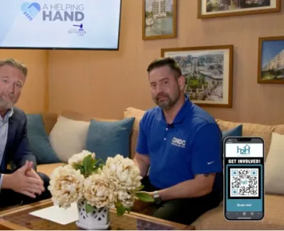 Two men seated in a living room set with A Helping Hand logo and a QR code on a phone for involvement