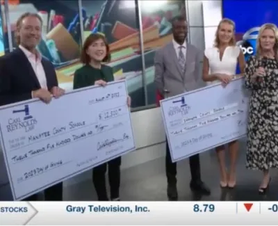 Five people on a news set holding large donation checks for Manatee County Schools and the Salvation Army Tampa division.