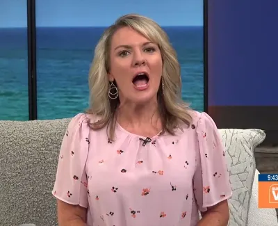 Female TV presenter in pink blouse speaking on a set with ocean view background and Suncoast View logo